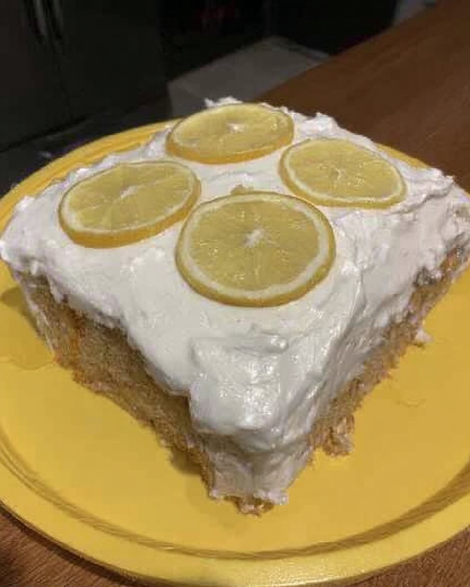 Whole lemon cake on a stand next to a cup of tea
