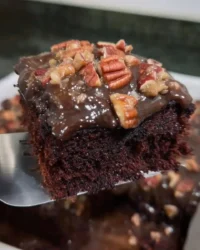 Slice of old fashioned chocolate cake with pecan icing on a white plate