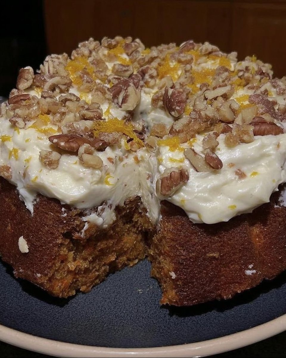 Slice of carrot cake topped with pecans on a ceramic plate
