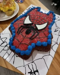 Spider Man cake shaped like a mask with red fondant and webbing details