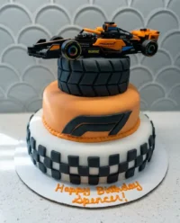 A completed F1 race car cake with apricot icing and liquorice tires on a black board.