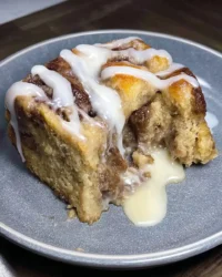 A rustic cinnamon roll cake served in a baking dish on a weathered wooden farmhouse table.