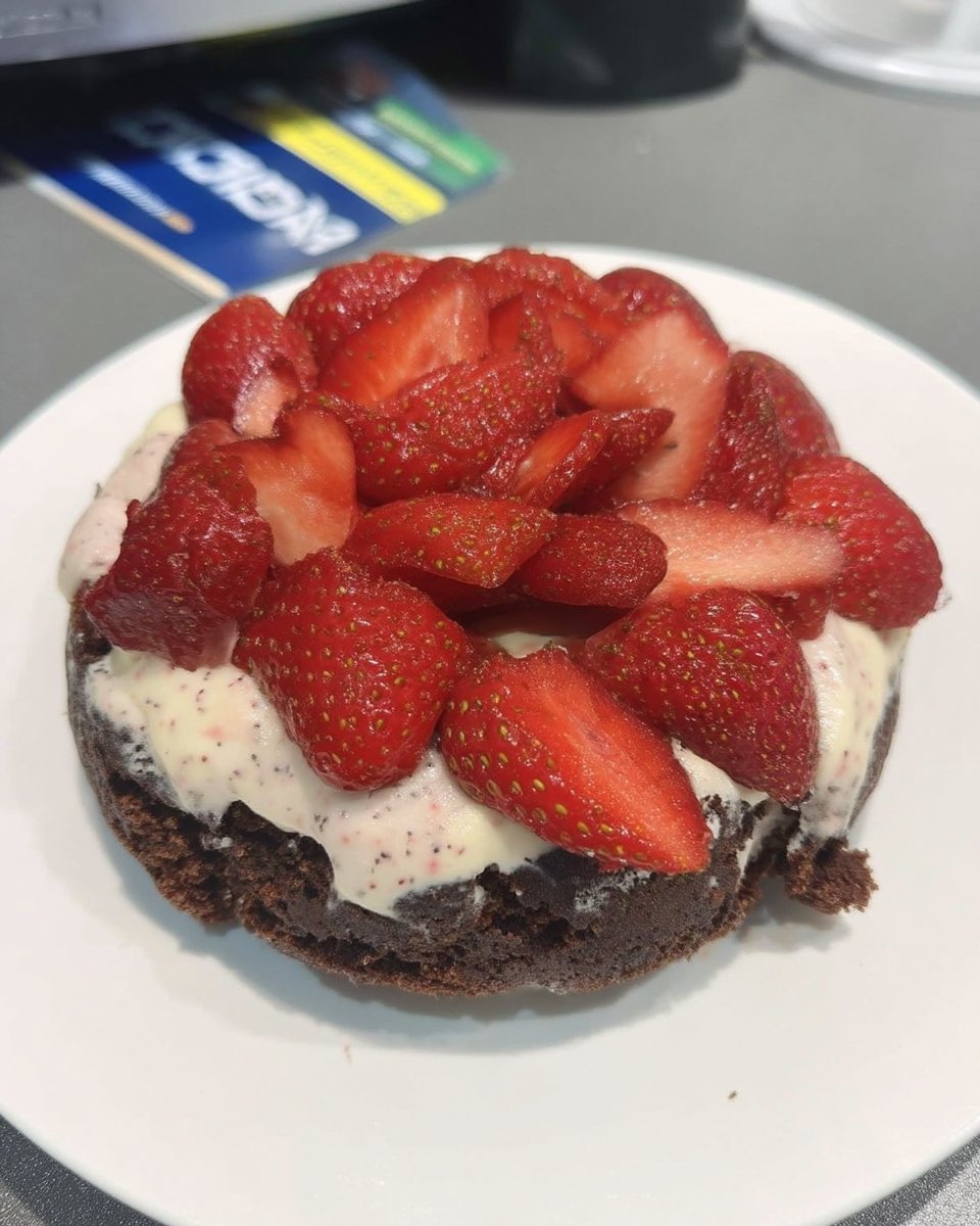 A person spreading pink strawberry buttercream onto a dark chocolate cake layer.
