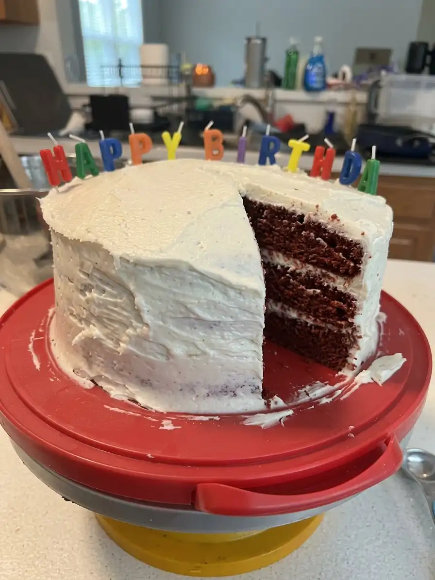 A person spreading white cream cheese frosting onto a red cake layer