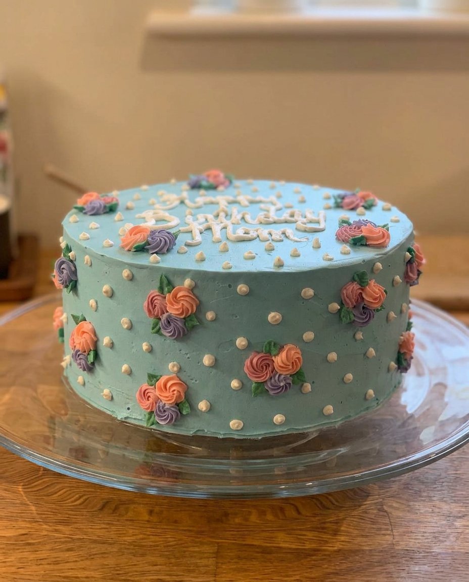 A 5 inch tall white cake decorated with palette knife roses and daisies for a Happy Birthday Mom Cake.