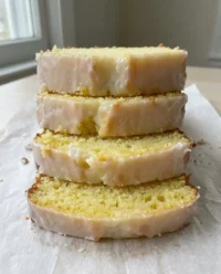 A golden lemon pound cake with thick white icing on a wooden board