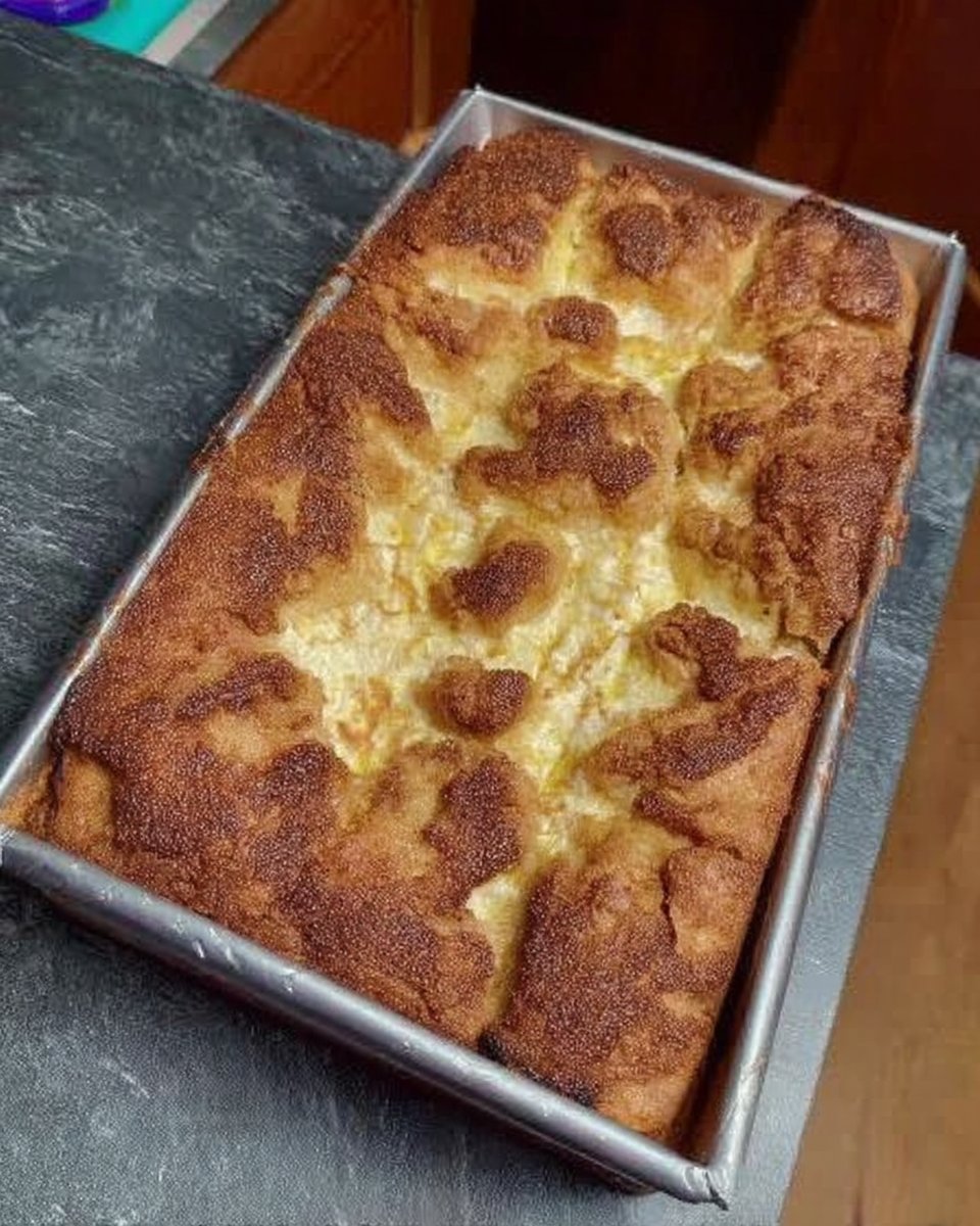 A golden brown ooey gooey butter cake resting on a wire cooling rack in a kitchen.