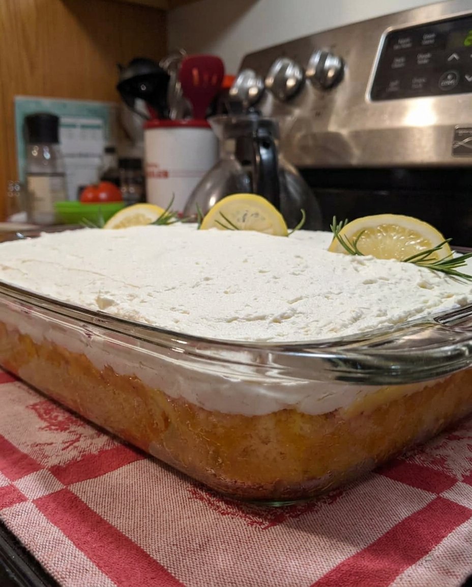 A rustic lemon poke cake with a sugary glaze sitting on a wooden farmhouse table.