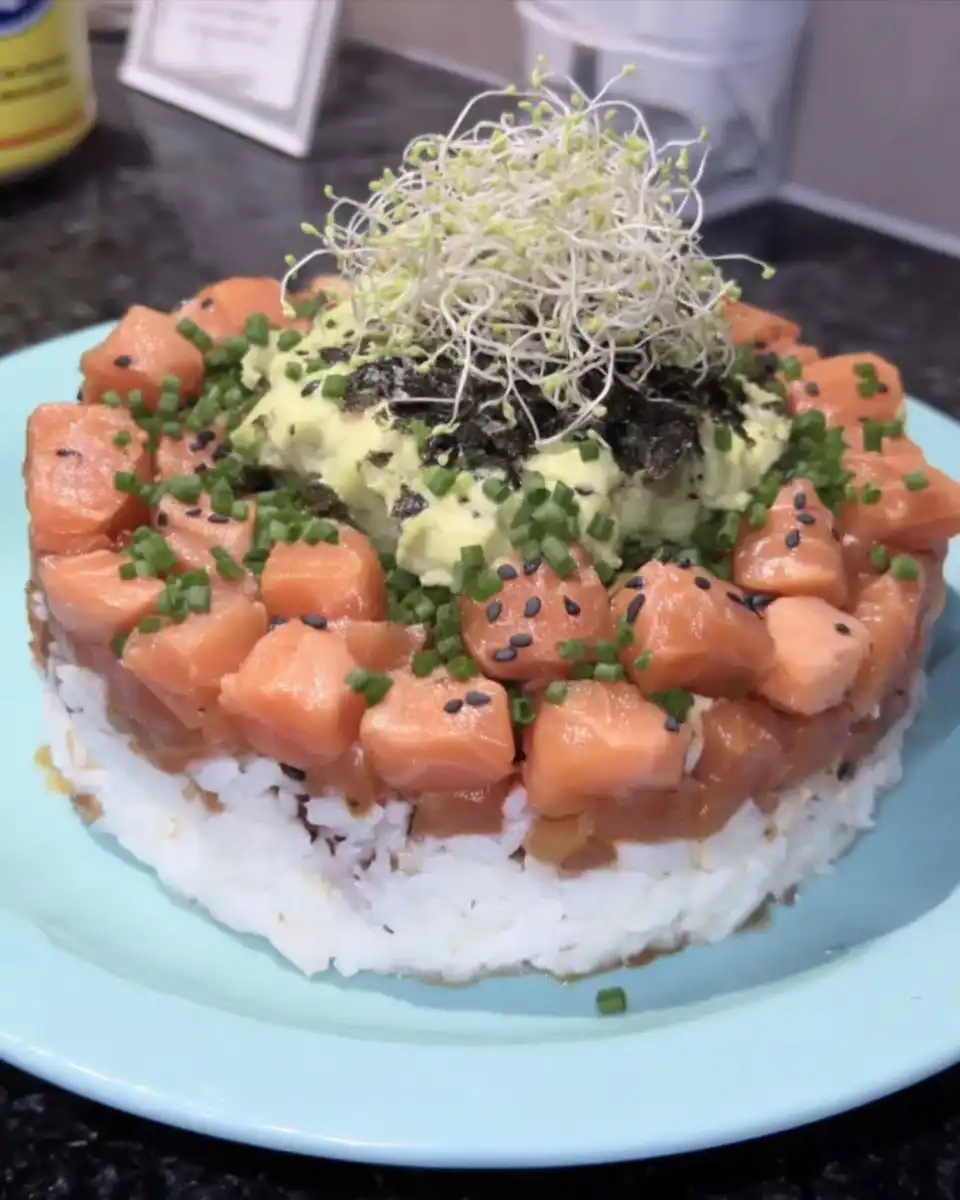 A completed sushi cake on a dark ceramic platter with sesame seeds