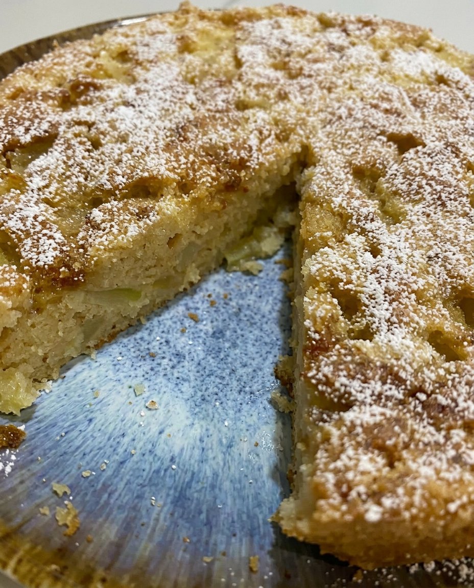 A sliced piece of apple cake with a dusting of sugar