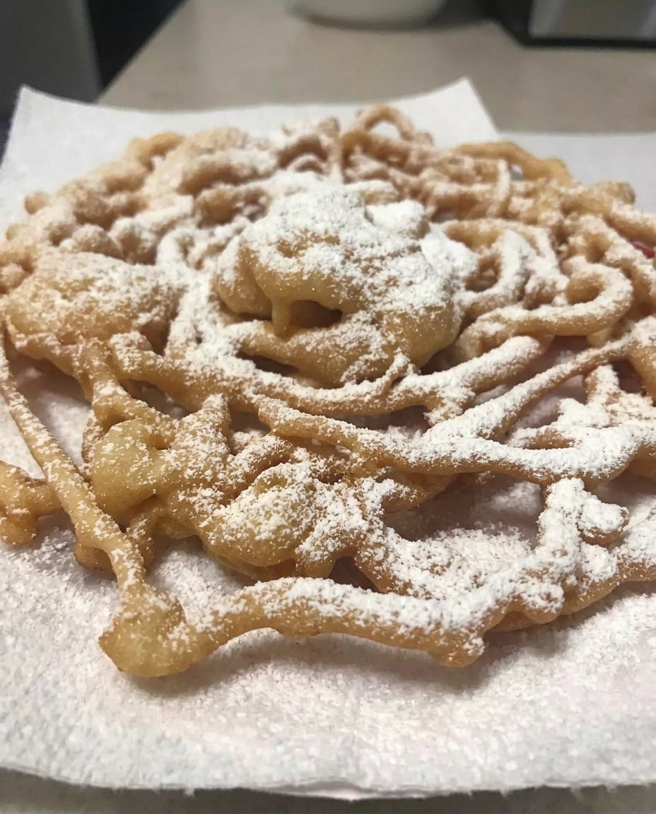 A golden brown funnel cake generously dusted with powdered sugar on a white plate.