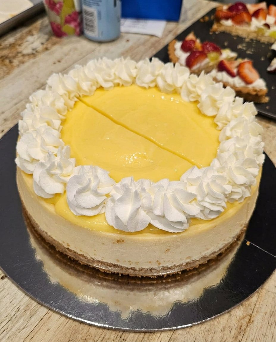 A clean slice of lemon cheesecake on a plate with fresh raspberries and a mint leaf.