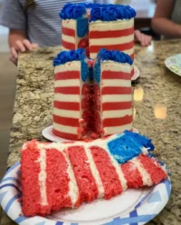 A four-layer vanilla cake decorated as an American flag with red white and blue smeared buttercream stars and stripes.