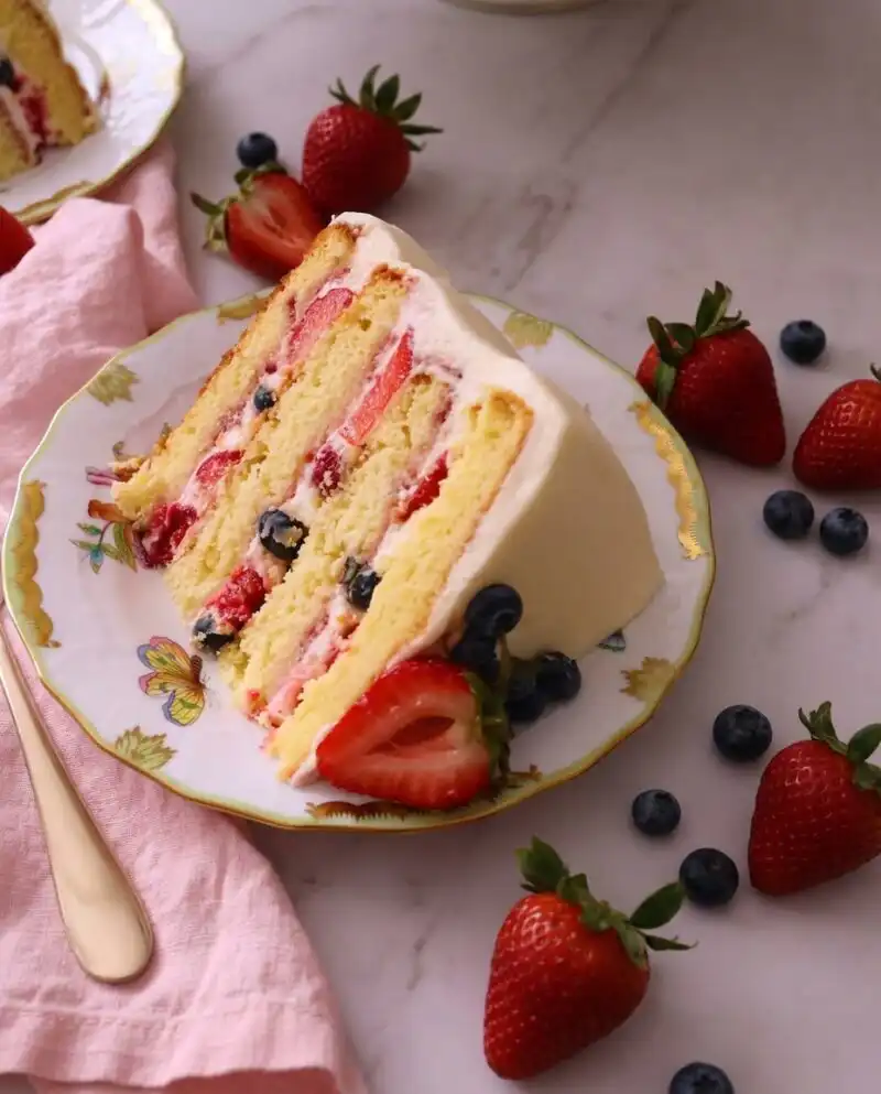 A tall layered Chantilly Bliss cake topped with fresh strawberries and blueberries