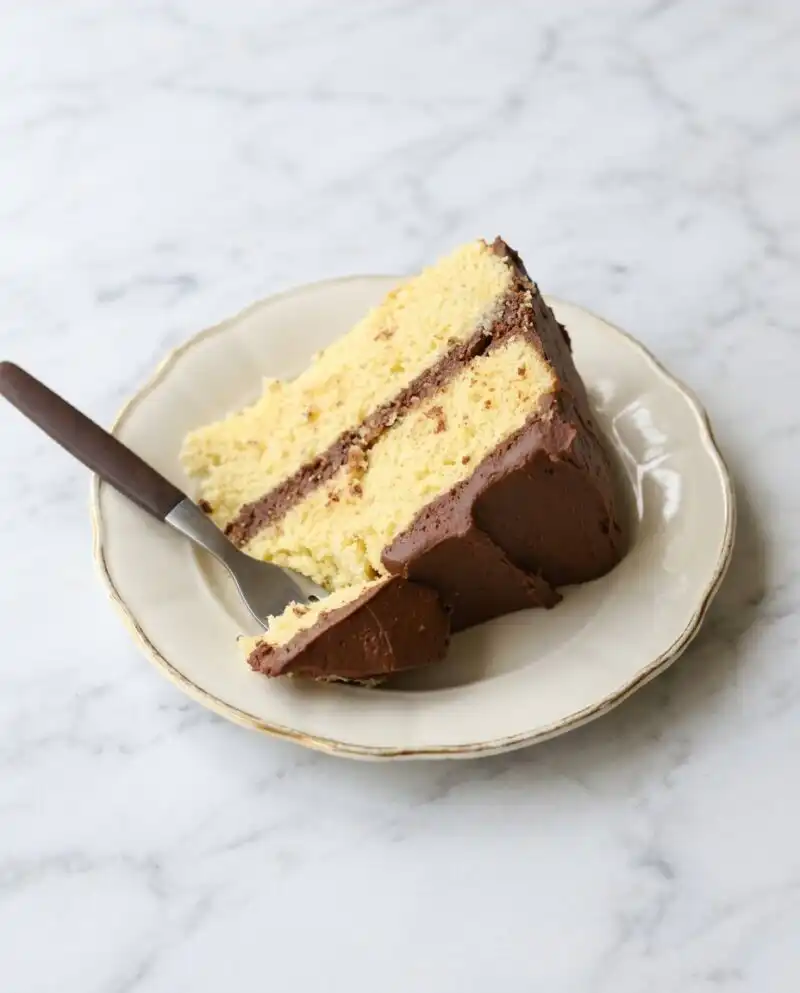 A Classic Two-Layer Yellow Cake with Chocolate Frosting sitting on a rustic wooden table.