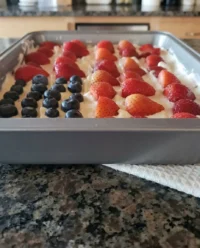 A beautiful no-bake American flag cheesecake with cherry and blueberry toppings on a wooden picnic table.