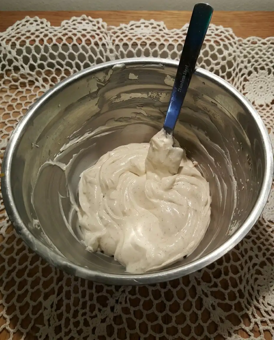 A close up of a spatula folding sliced strawberries and blueberries into a white creamy base