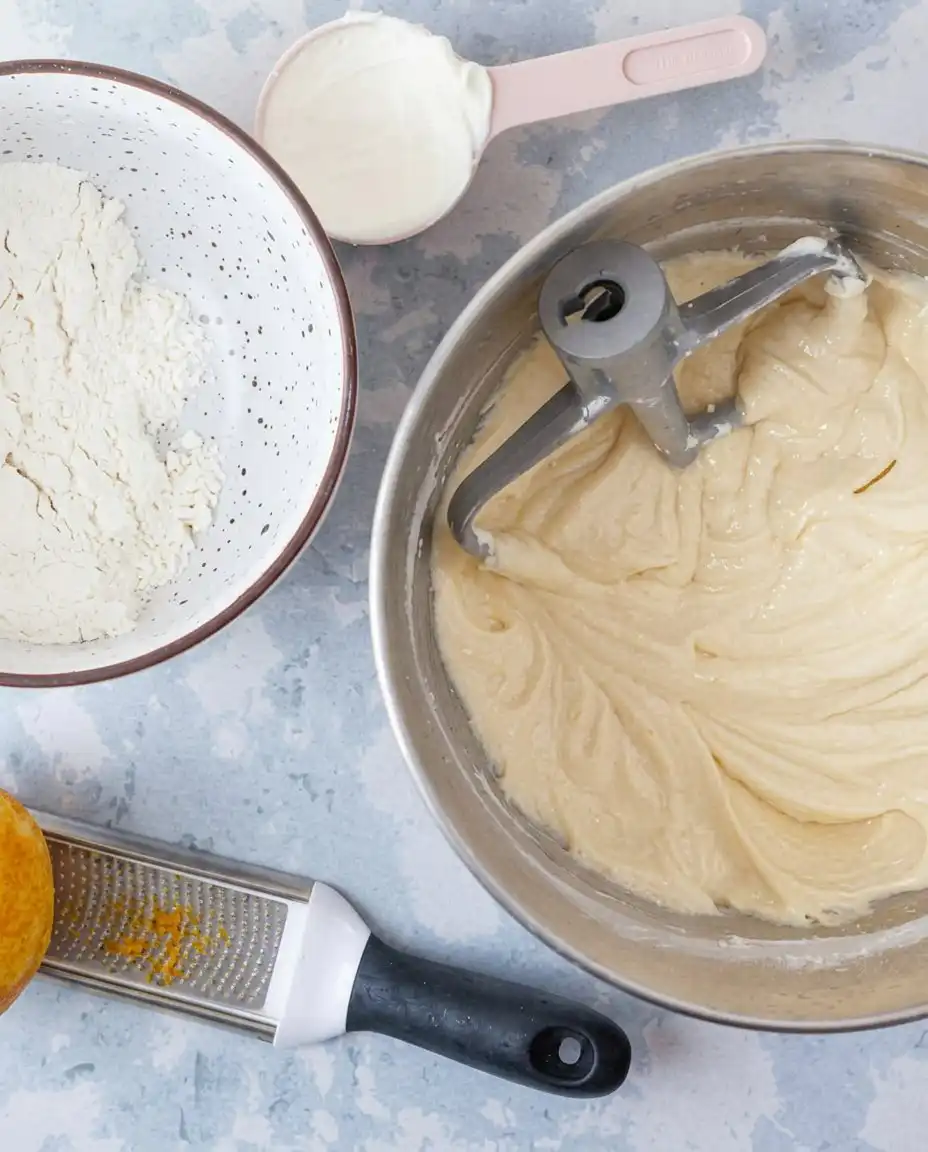 Bowls of flour, eggs, fresh lemons, and mascarpone cheese on a counter.