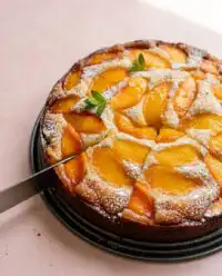 A golden brown Fresh Peach Cake resting on a wire cooling rack in a sunny kitchen.