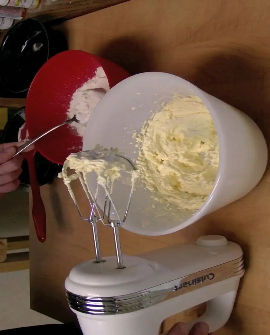 A bowl of fresh sliced peaches next to two sticks of unsalted butter and a bag of flour.