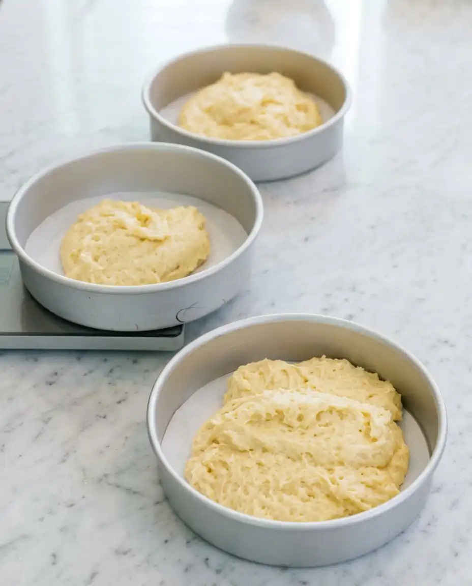 Creamy lemon frosting being applied to the layers of a Blackberry Lemon Cake with an offset spatula.