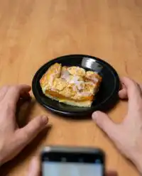 A golden brown slice of Peach Coffee Cake resting on a white ceramic pedestal plate.