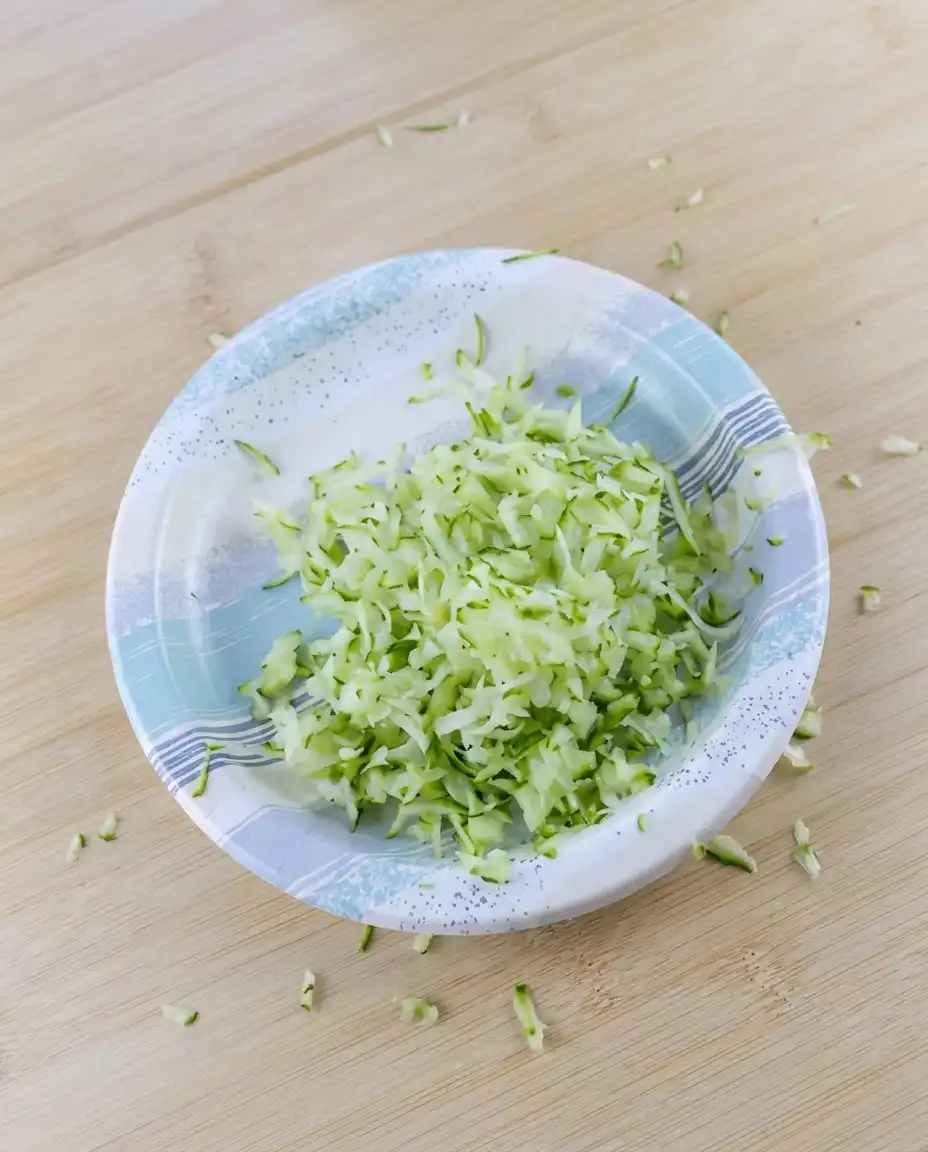 Bowls of flour, grated zucchini, and diced apples for apple zucchini bread on a counter.