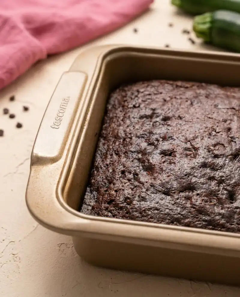 A thick slice of Moist Chocolate Zucchini Cake sitting on a rustic wooden cutting board.