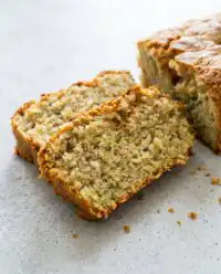 A thick slice of moist Lemon Zucchini Cake with white glaze on a rustic plate.