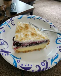 A layered no bake lemon blueberry dessert in a clear glass baking dish on a rustic table