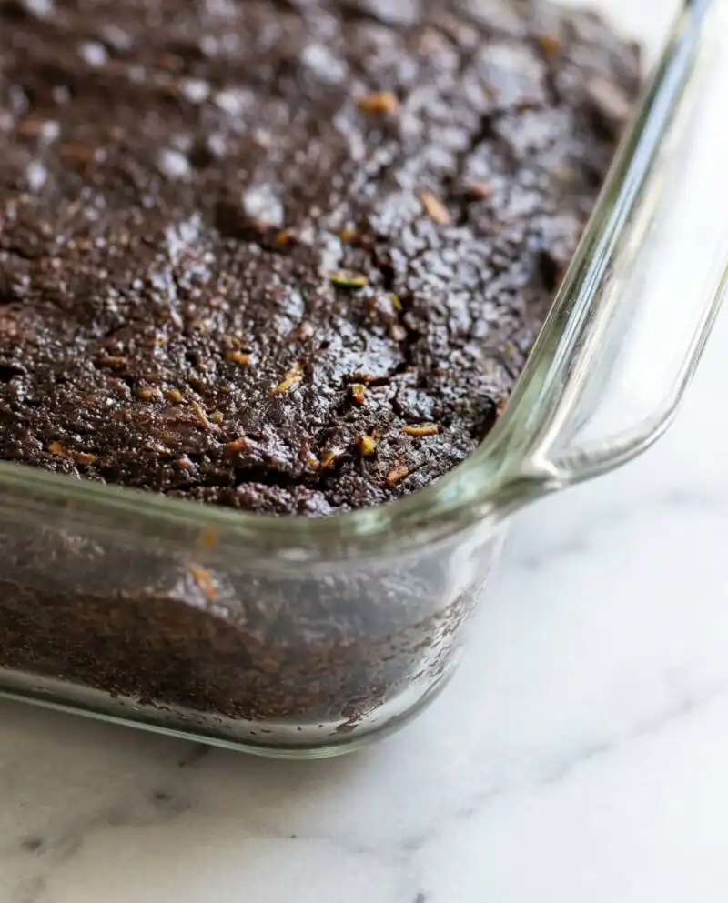 A thick slice of Old-Fashioned Chocolate Zucchini Cake resting on a rustic wooden board in a farmhouse kitchen.