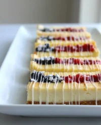 Festive patriotic cheesecake bars topped with fresh strawberries and blueberries in a flag pattern