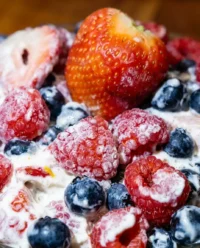 A large glass bowl filled with red white and blue cheesecake salad featuring strawberries and blueberries