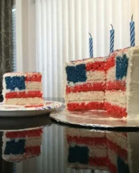 A tall red white and blue layered flag cake on a rustic wooden table