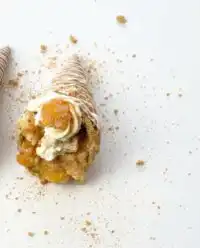 A group of golden Peach Cobbler Cheesecake Cones arranged on a rustic wooden platter.