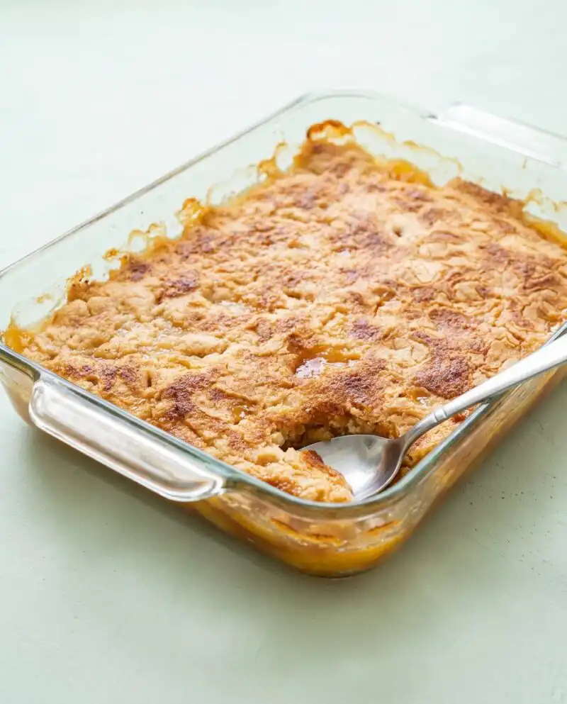 A golden brown Peach Cobbler with Yellow Cake Mix bubbling in a glass baking dish.