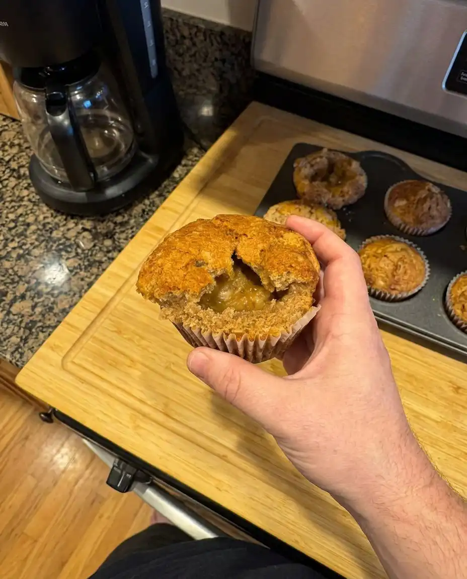 A silicone spatula lifting a thick, lumpy muffin batter with folded in peach pieces.
