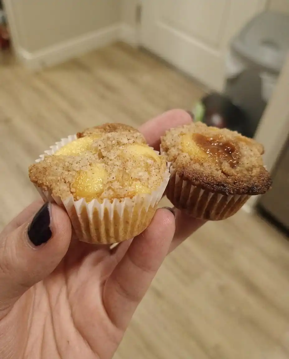 Close up of a peach muffin with a golden brown dome and visible fruit