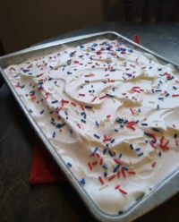 A festive Red, White & Blue Patriotic Poke Cake on a rustic wooden table.