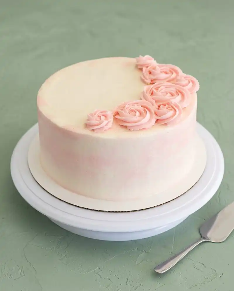 A three layer Rose Water Layer Cake cooling on a wire rack with a golden brown crust.