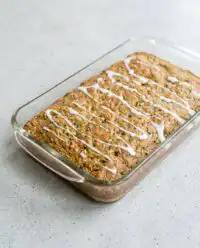 A slice of rustic Grandma's Zucchini Cake with cream cheese frosting on a white plate.