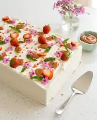 A rustic Best Strawberry Sheet Cake topped with fresh berries and mint on a wooden board.