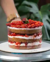 A rustic Strawberry Vanilla Cake with fresh berries sitting on a dark wooden cutting board.