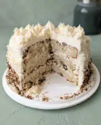 A Three-Layer Italian Cream Cake with cream cheese frosting and pecans on a rustic wooden table.