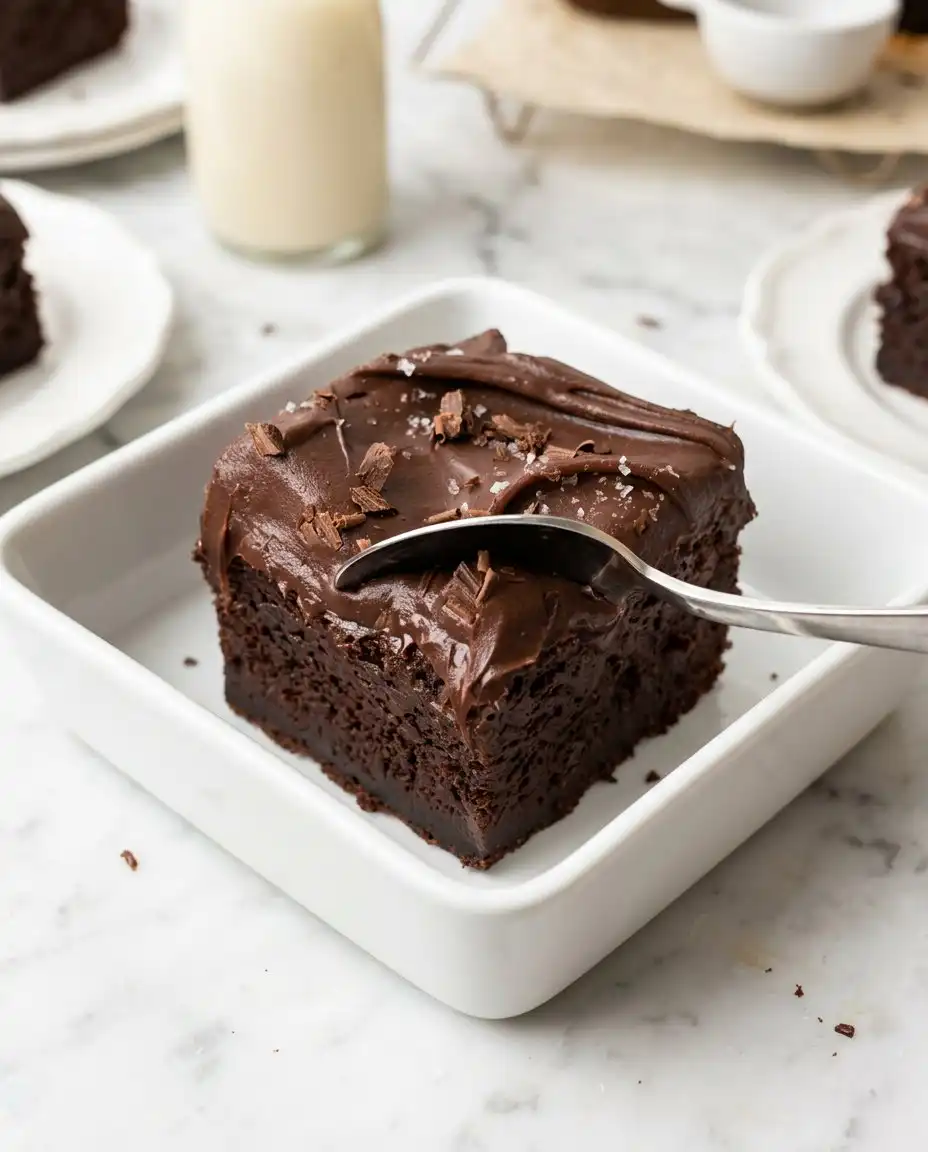 A square slice of Vegan Chocolate Zucchini Cake served on a white plate with a fork.