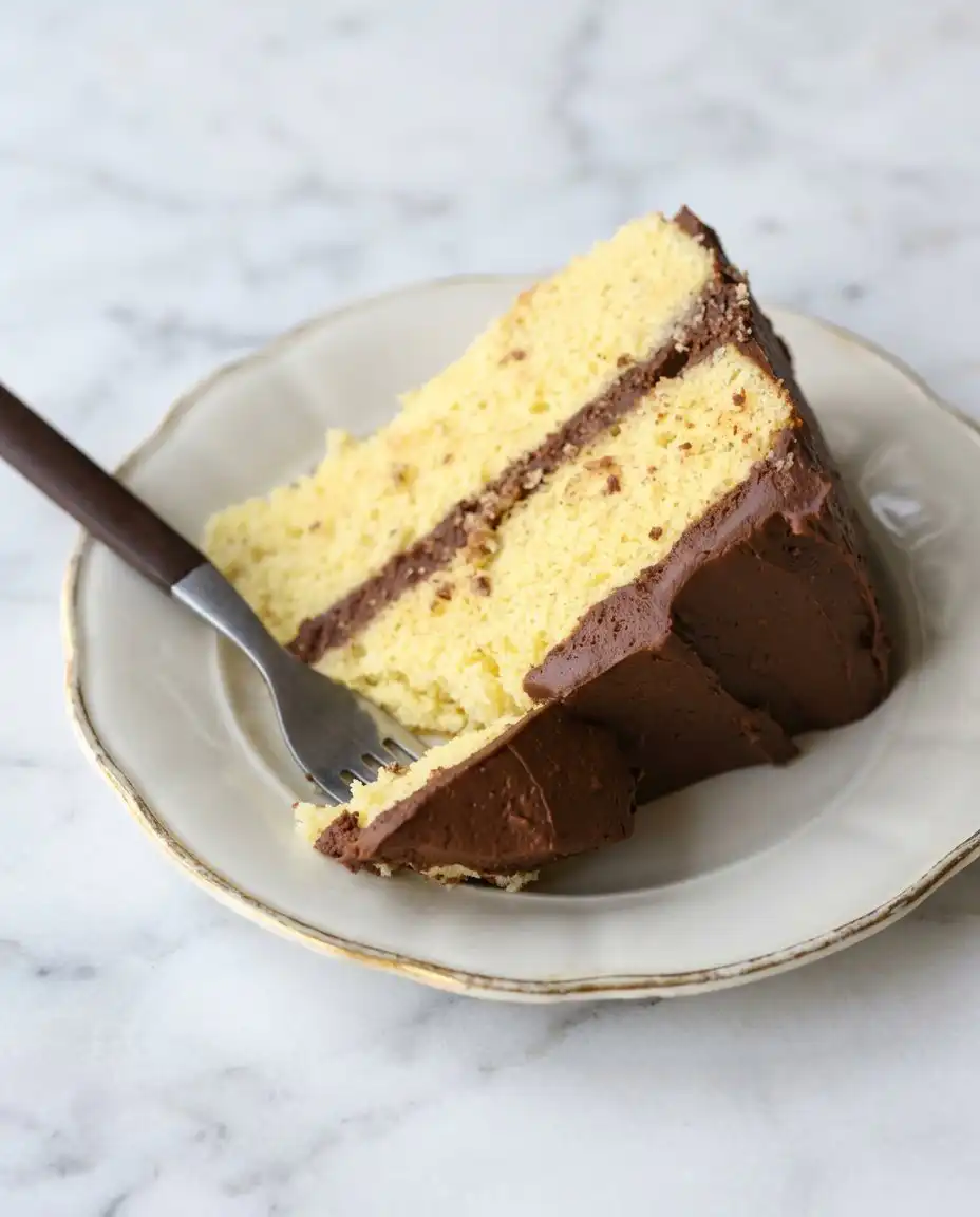 A single slice of Classic Two-Layer Yellow Cake with Chocolate Frosting on a linen napkin.