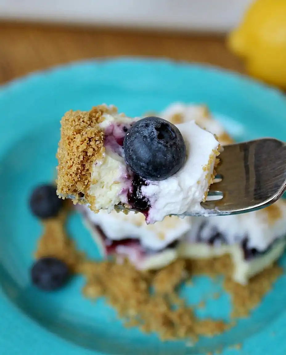 A close up of a slice of no bake lemon blueberry dessert being lifted from a dish