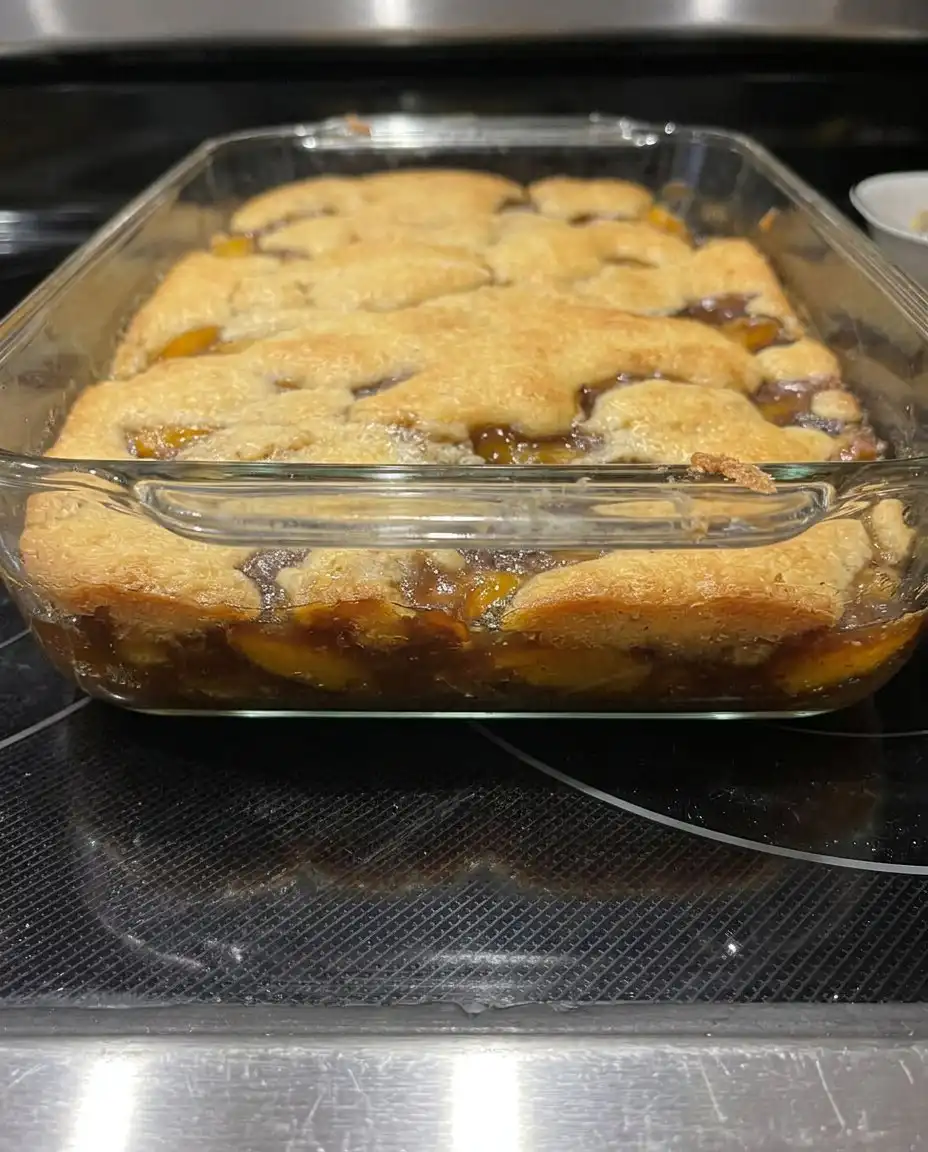A scoop of peach cobbler in a white bowl topped with melting vanilla ice cream
