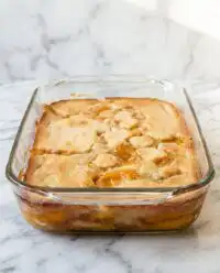A golden brown Peach Cobbler with Canned Peaches served in a glass baking dish.