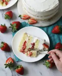 A rustic three layer strawberry shortcake cake topped with fresh strawberries on a wooden table